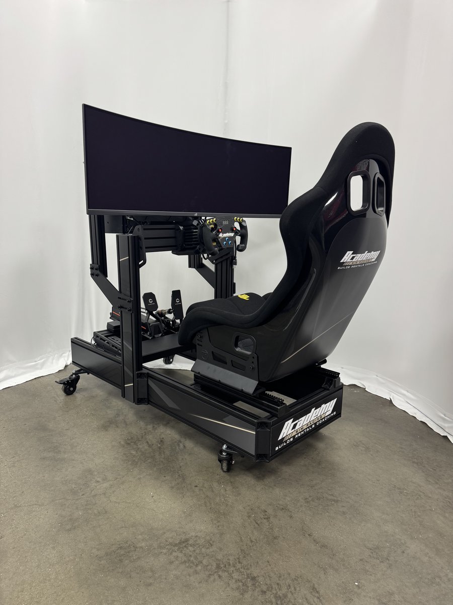 Full view of the Academy racing simulator rig — Simucube pedals, formula-style wheel, fixed racing seat on a rolling aluminium frame